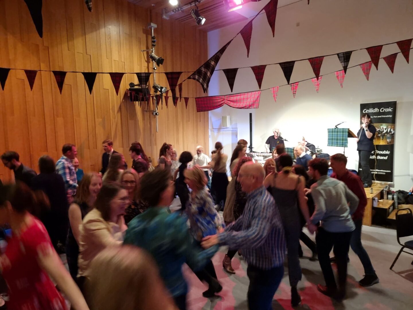 Group of people dancing in pairs, while a band plays on stage.