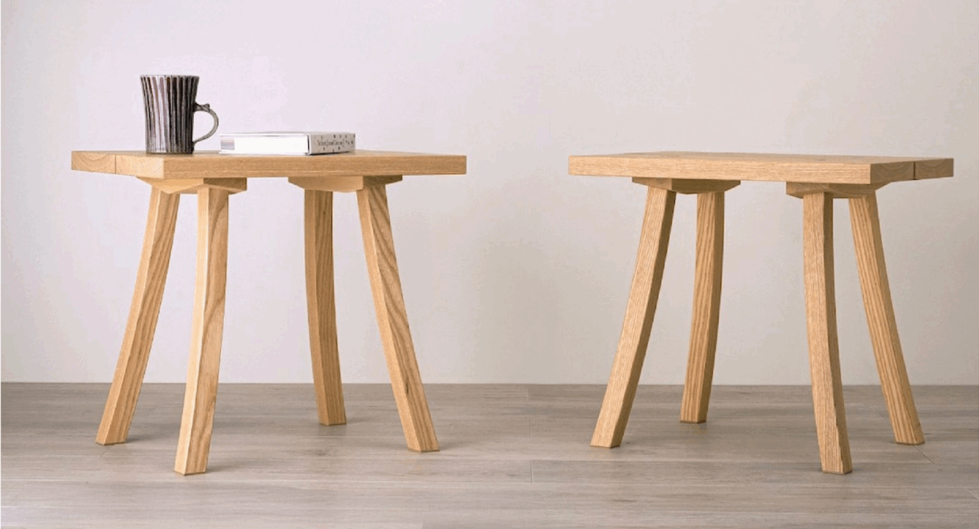 2 small wooden tables. On one of the tables there is a book and a mug.
