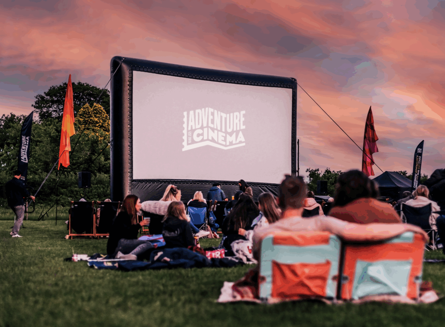 Groups of people sitting outdoors, while looking at a large cinema screen.