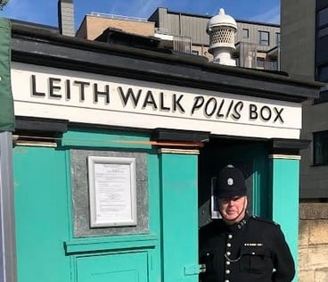 A police officer in historical uniform outside the green-painted polisbox
