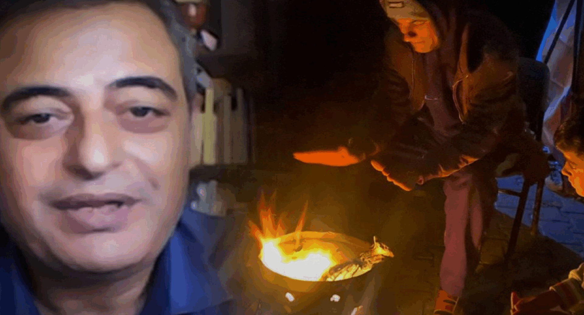 A man looking at the camera and a person warming up over a fire