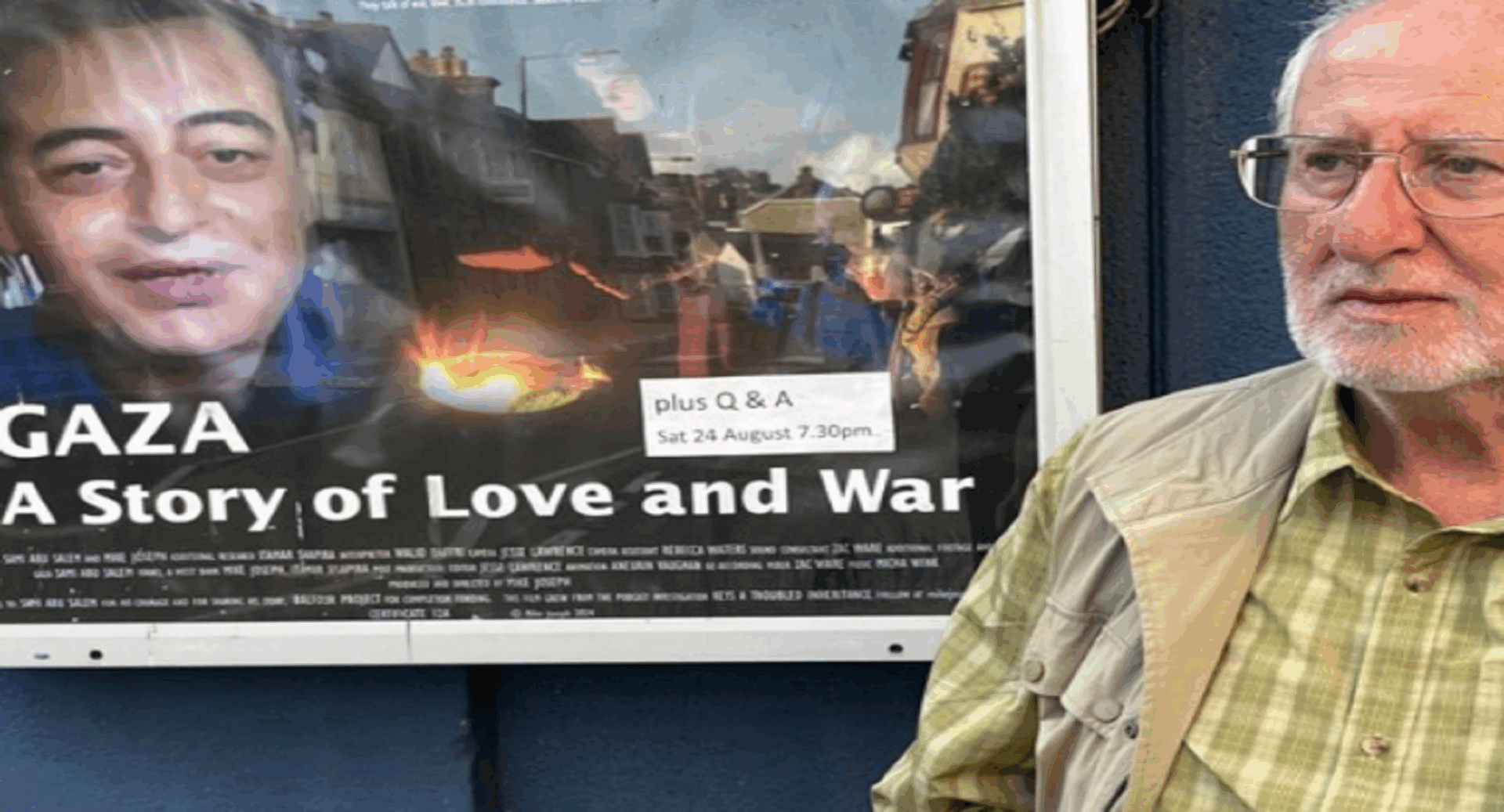 An older man standing beside a poster for Gaza: A Story of Love and War