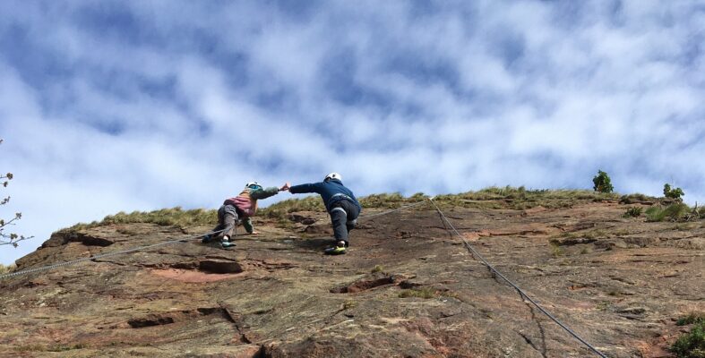 Father and daughter fist bumping on rockface with Height Club