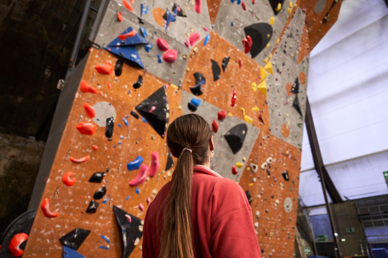 Lady staring up the face of an indoor Rock Climbing Wall