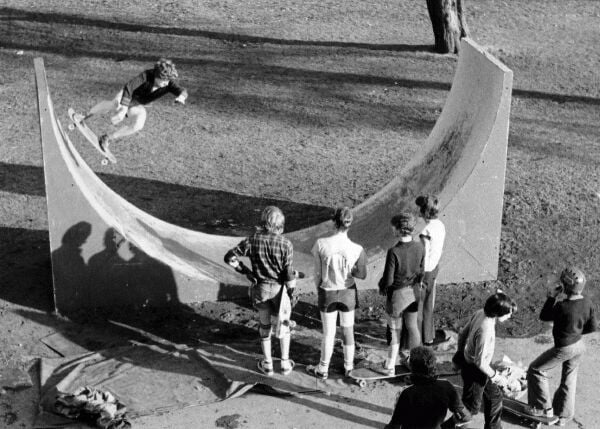 A black and white image of kids watching another skateboarding in a park in the 1980s