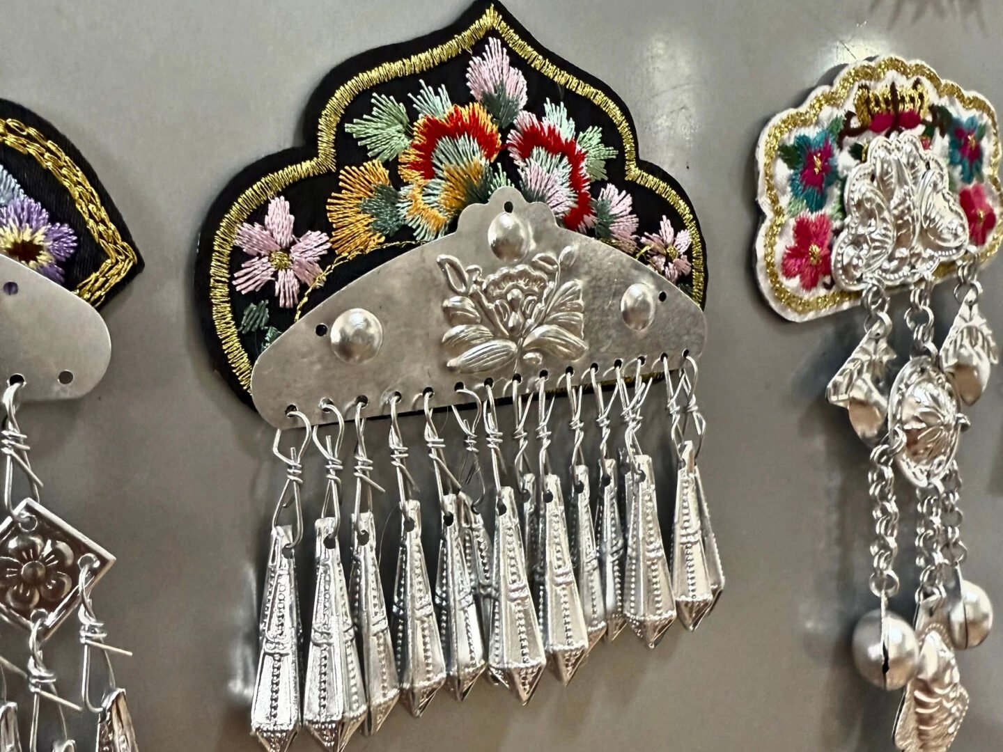 A decorative Chinese ornament with tear shaped silver tassels and embroidered flowers on a black background above