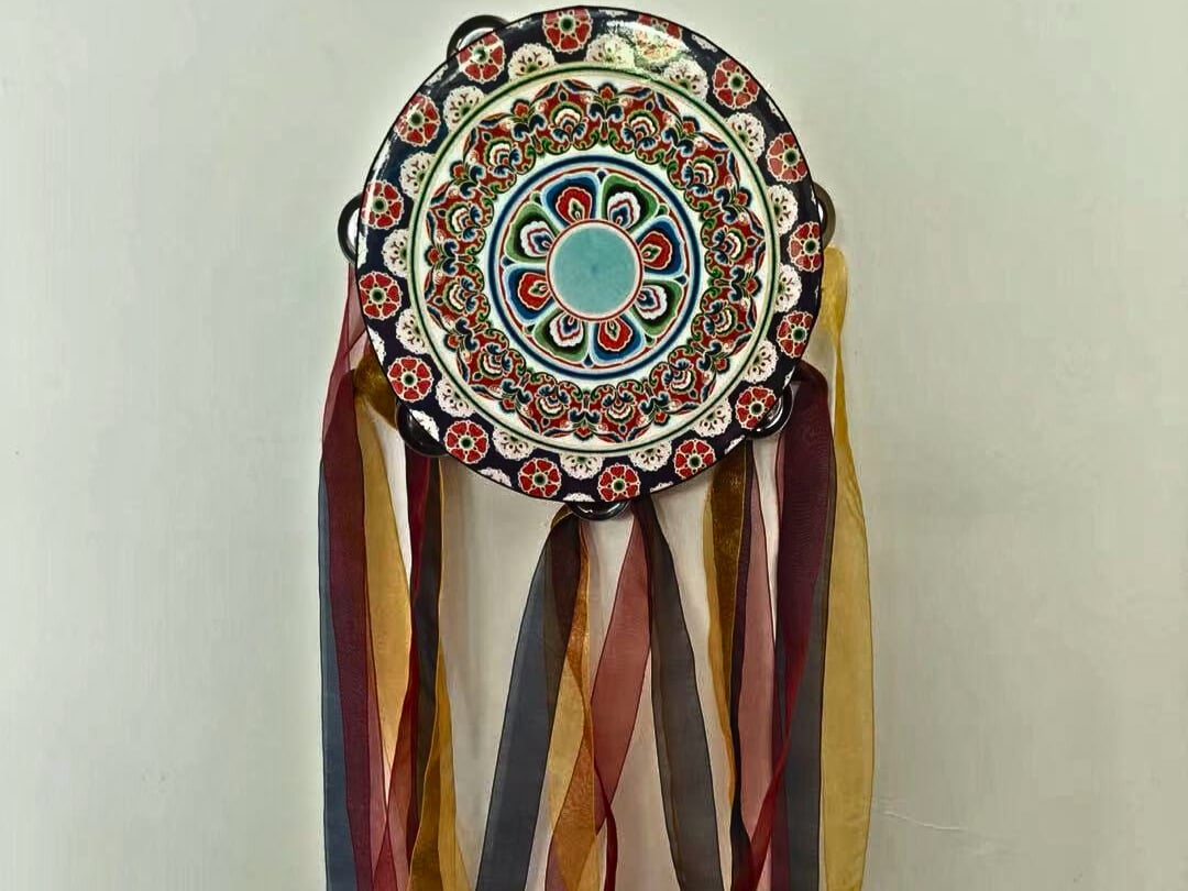 A red, blue and white circular plate with floral decorations and ribbon tassels dangling