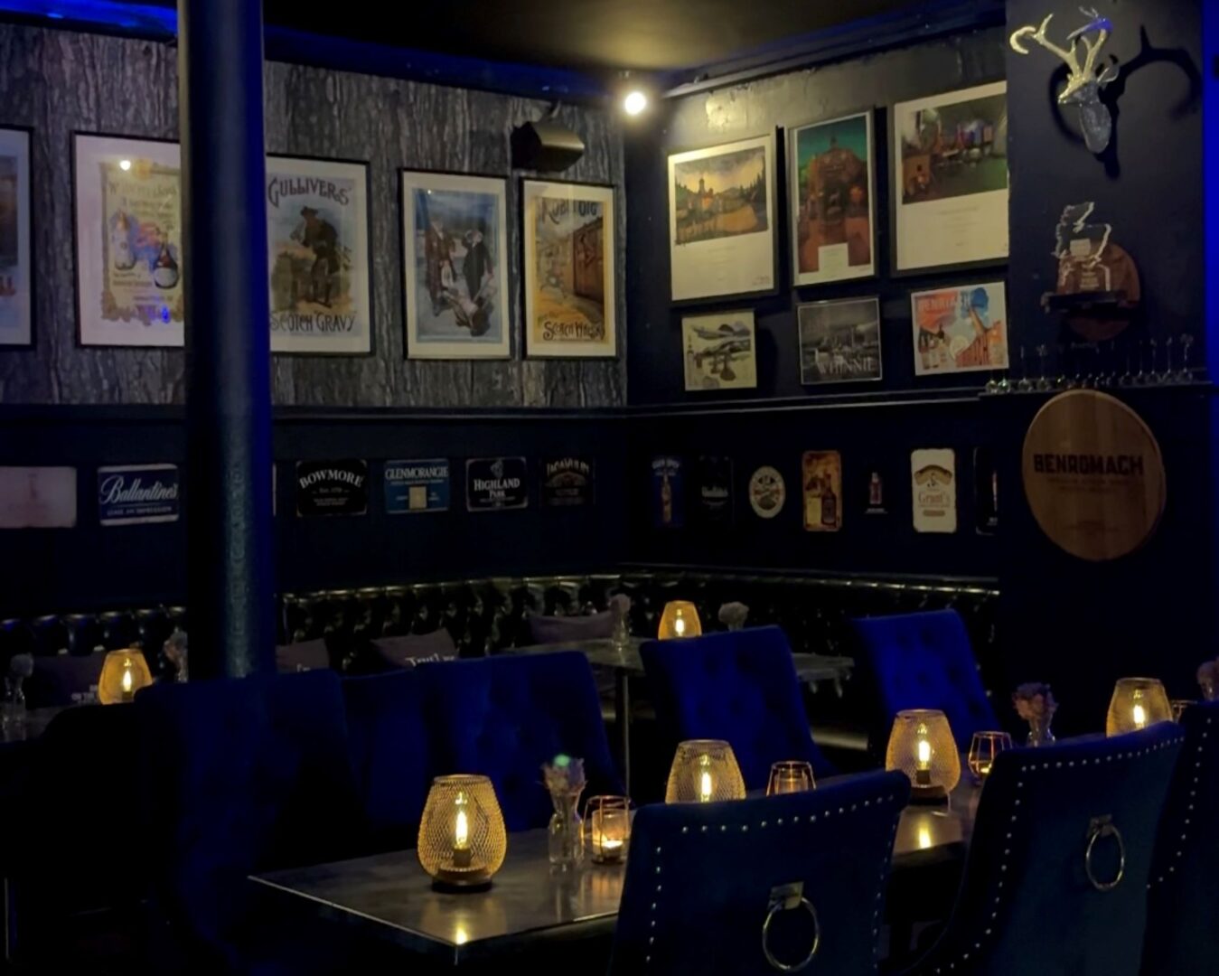 Bar area with tables and chairs. On each table there are candle-lit lanterns. Framed prints hang on the walls.