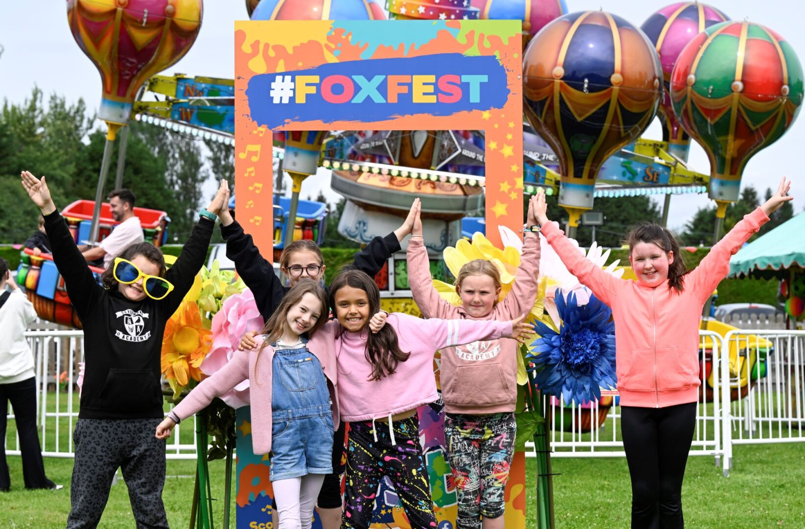 Group of young children standing in front of a fairground ride.