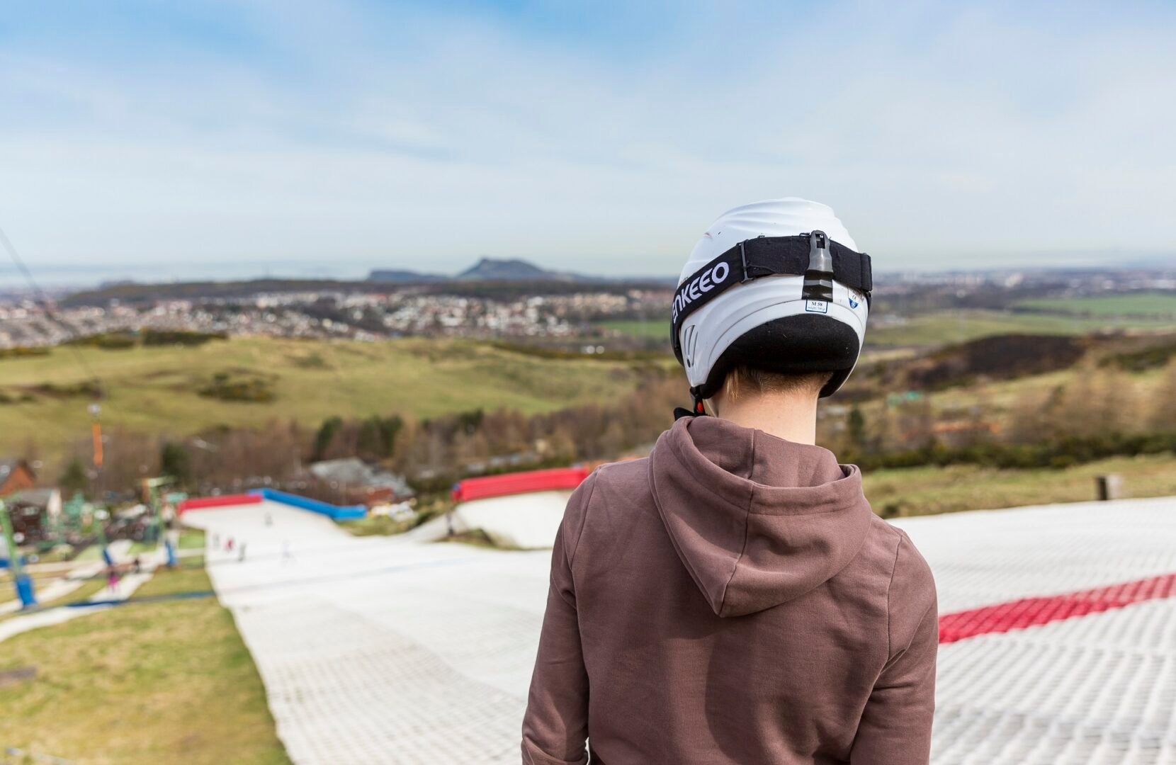 Skier staring down the dry ski slope at Hillend with Edinburgh skyline in distance