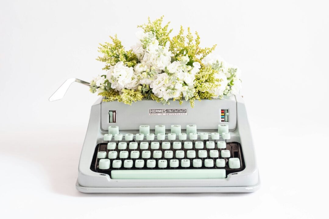 A manual typewriter with white flowers behind