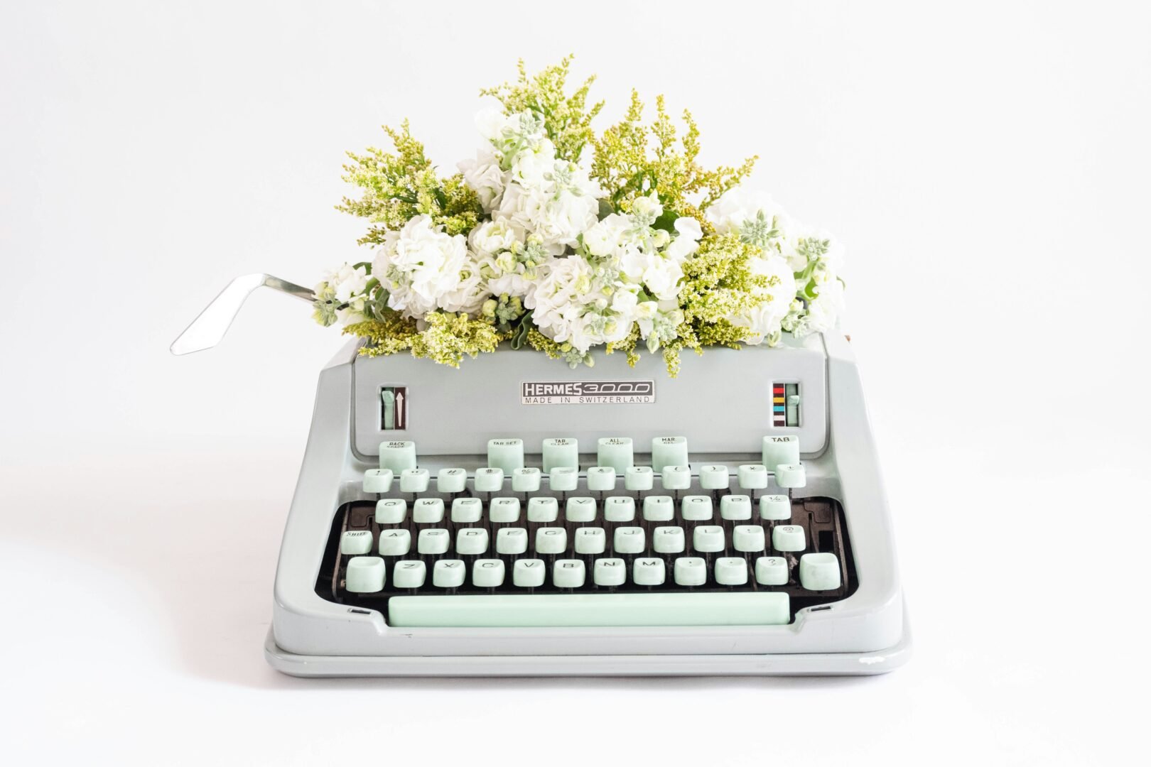 A manual typewriter with white flowers behind