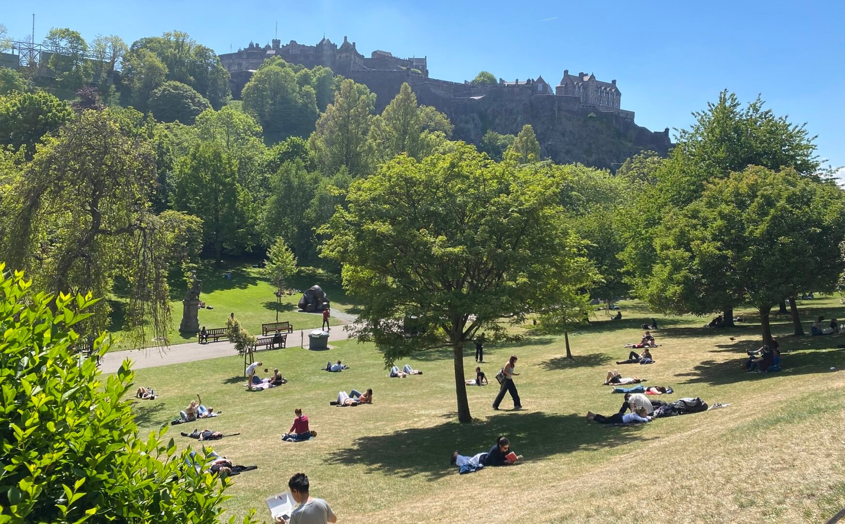 Princes Street Gardens with people sitting i the sun adn view of castle in background
