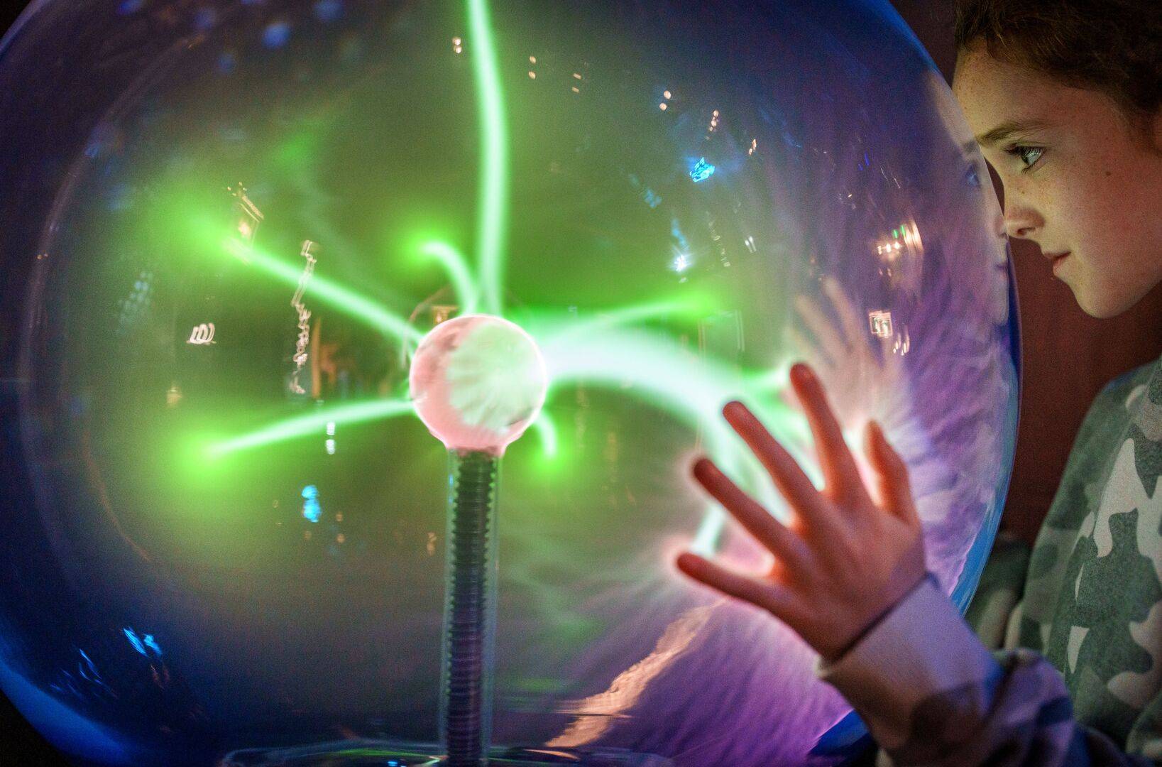 A young girl touches and looks into a glass ball with green electric light beams. The Electric Room, at Camera Obscura & World of Illusions, Edinburgh.,© Camera Obscura & World of Illusions, Edinburgh