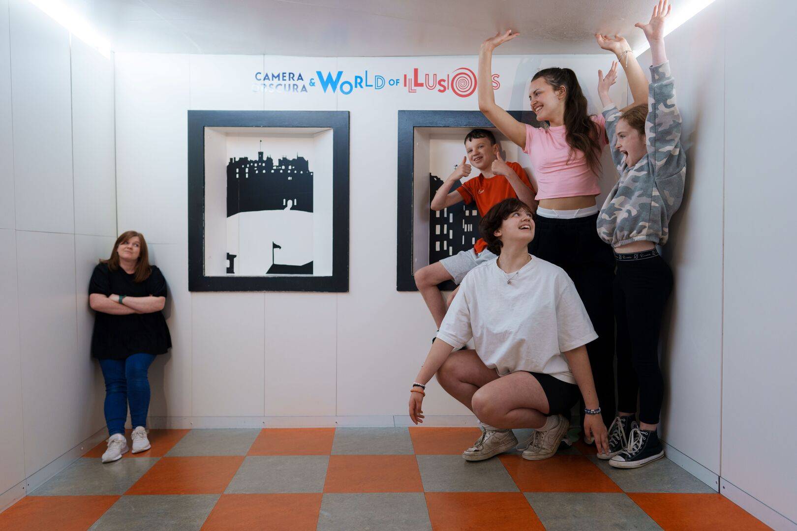 A mother and children appear overly small and overly tall in a white room. The Ames Room, Camera Obscura & World of Illusions, Edinburgh.,© Camera Obscura & World of Illusions, Edinburgh