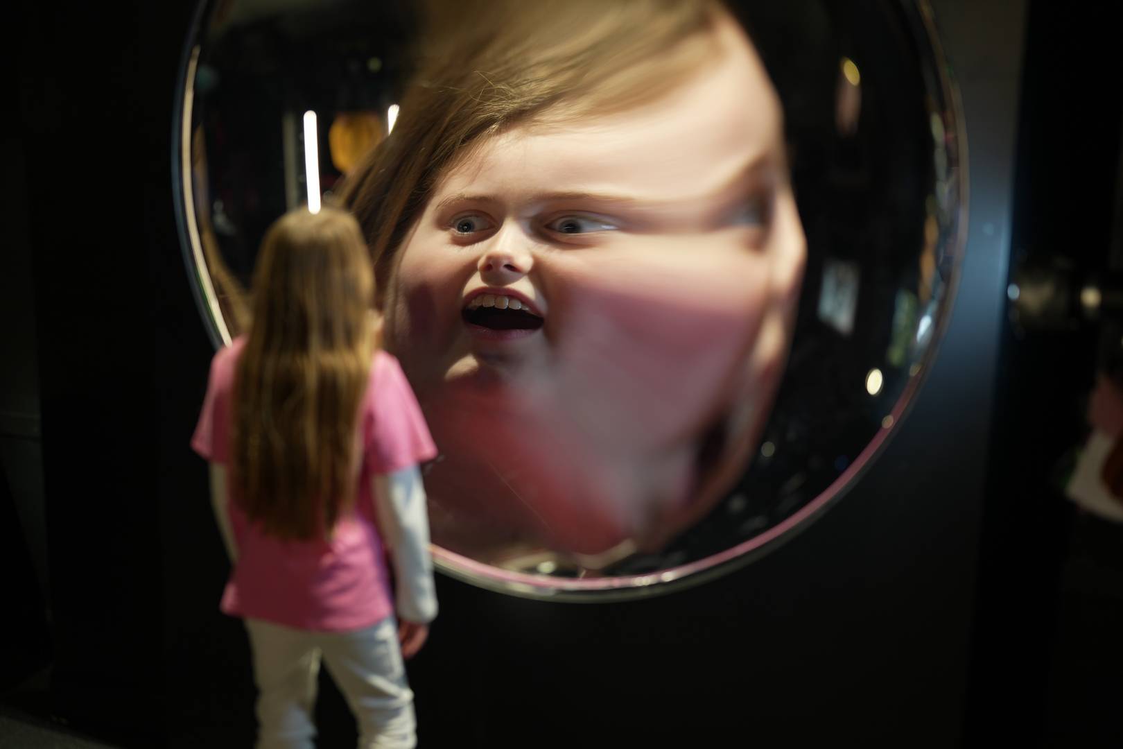 A young girl looks into a large round mirror which has distorted her face. Camera Obscura & World of Illusions, Edinburgh,© Camera Obscura & World of Illusions, Edinburgh