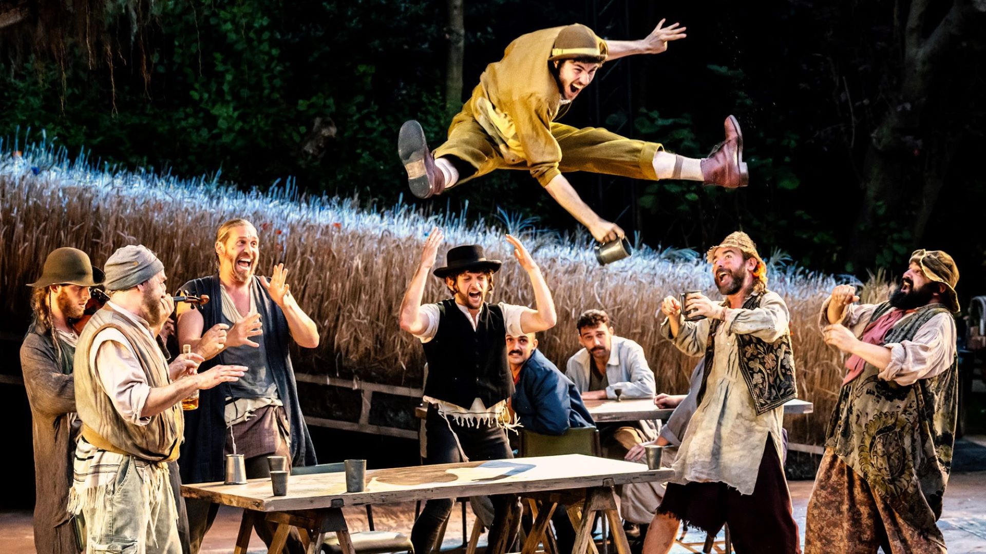 Group of men cheering on another man as he jumps over a table.