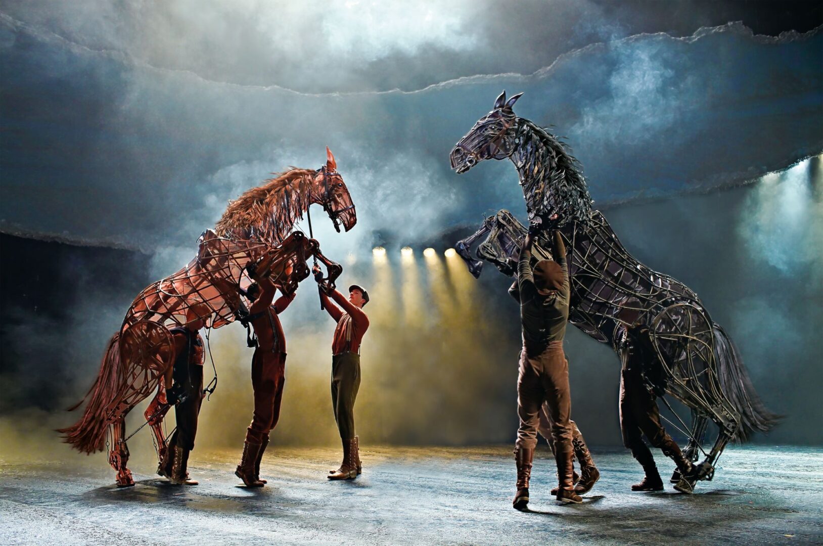 People reaching up to touch puppet horses, which are standing on their hind legs.
