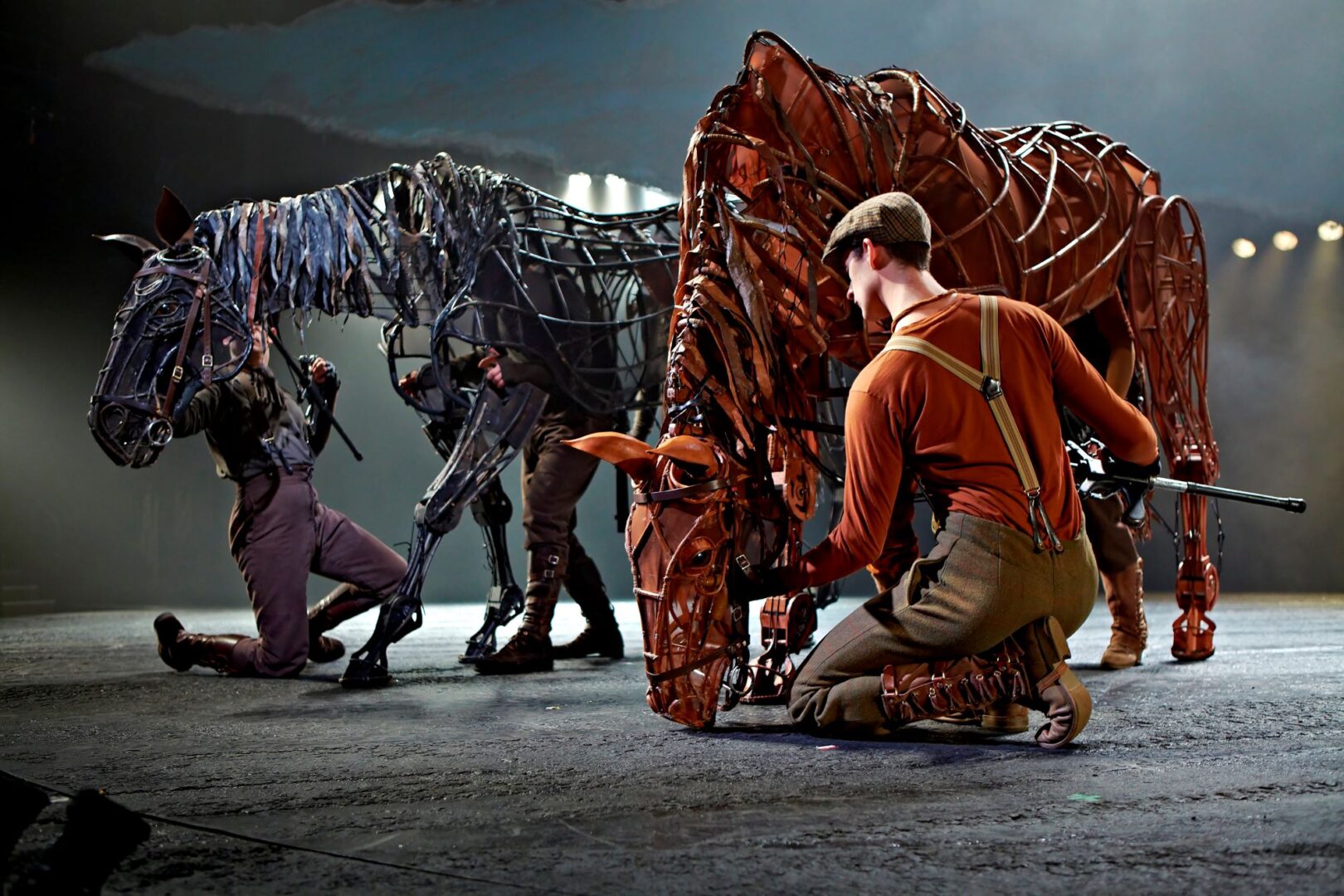 2 people crouching beside puppet horses.