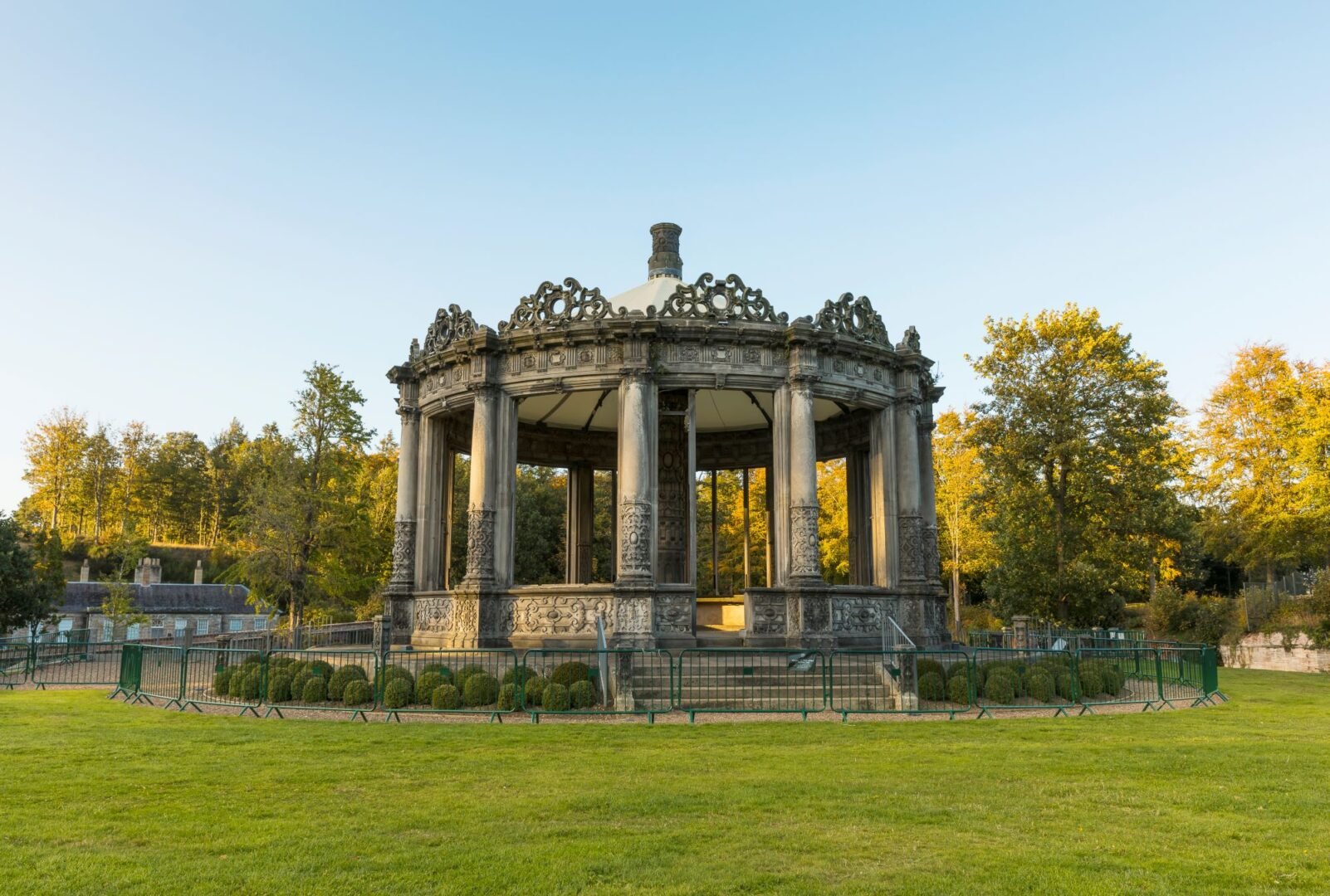An ornate outdoor round building, with bushes and trees surrounding it.