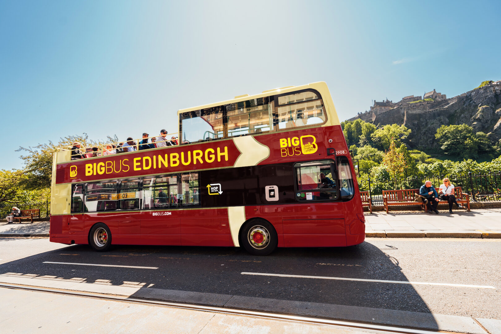 A red Big Bus travelling along Princes Street on a sunny day
