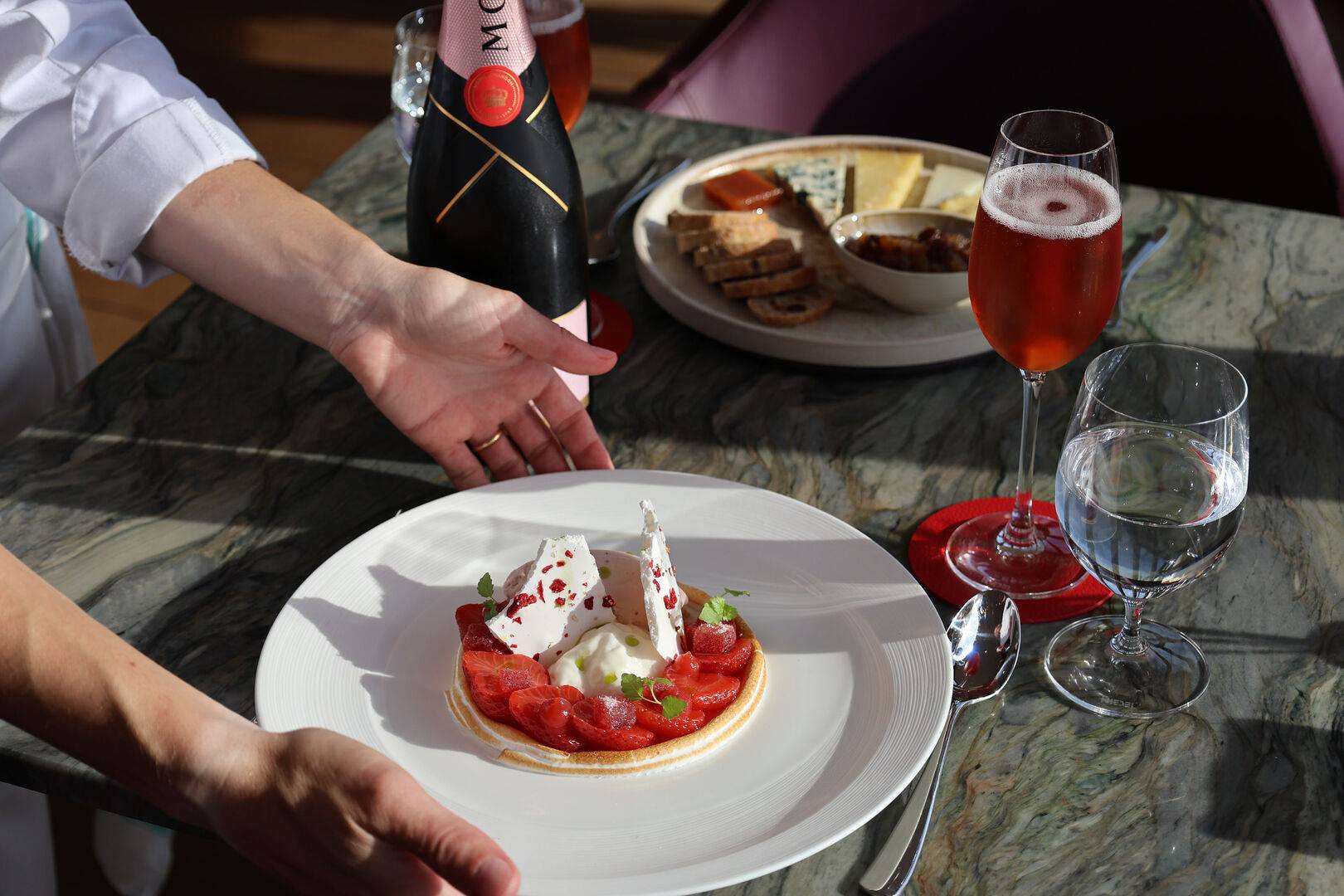 A Chef placing a strawberry and meringue dessert onto the table. There are glasses of rose Chapagne and a bottle of Moet & Chandon Champagne on the table too. ,© Latasha Millette