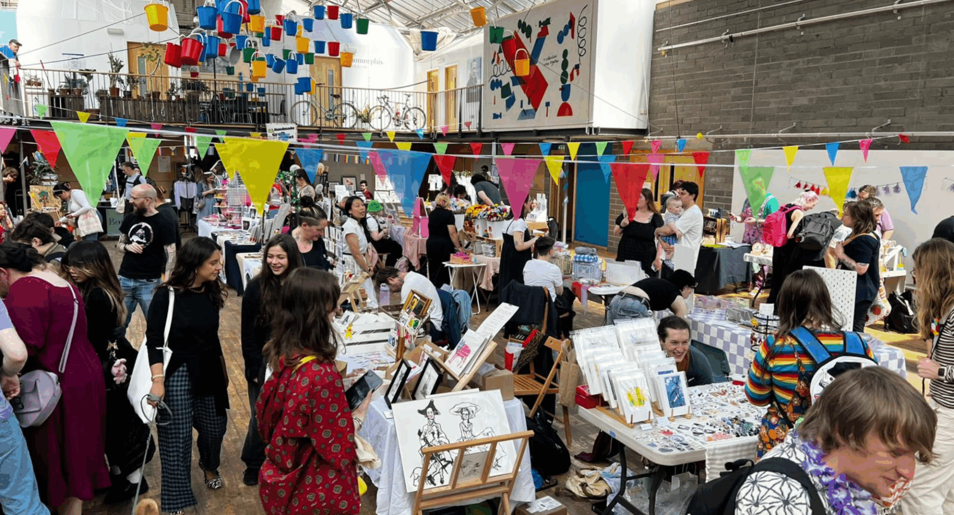 Groups of people in a large hall, looking at shopping stalls.