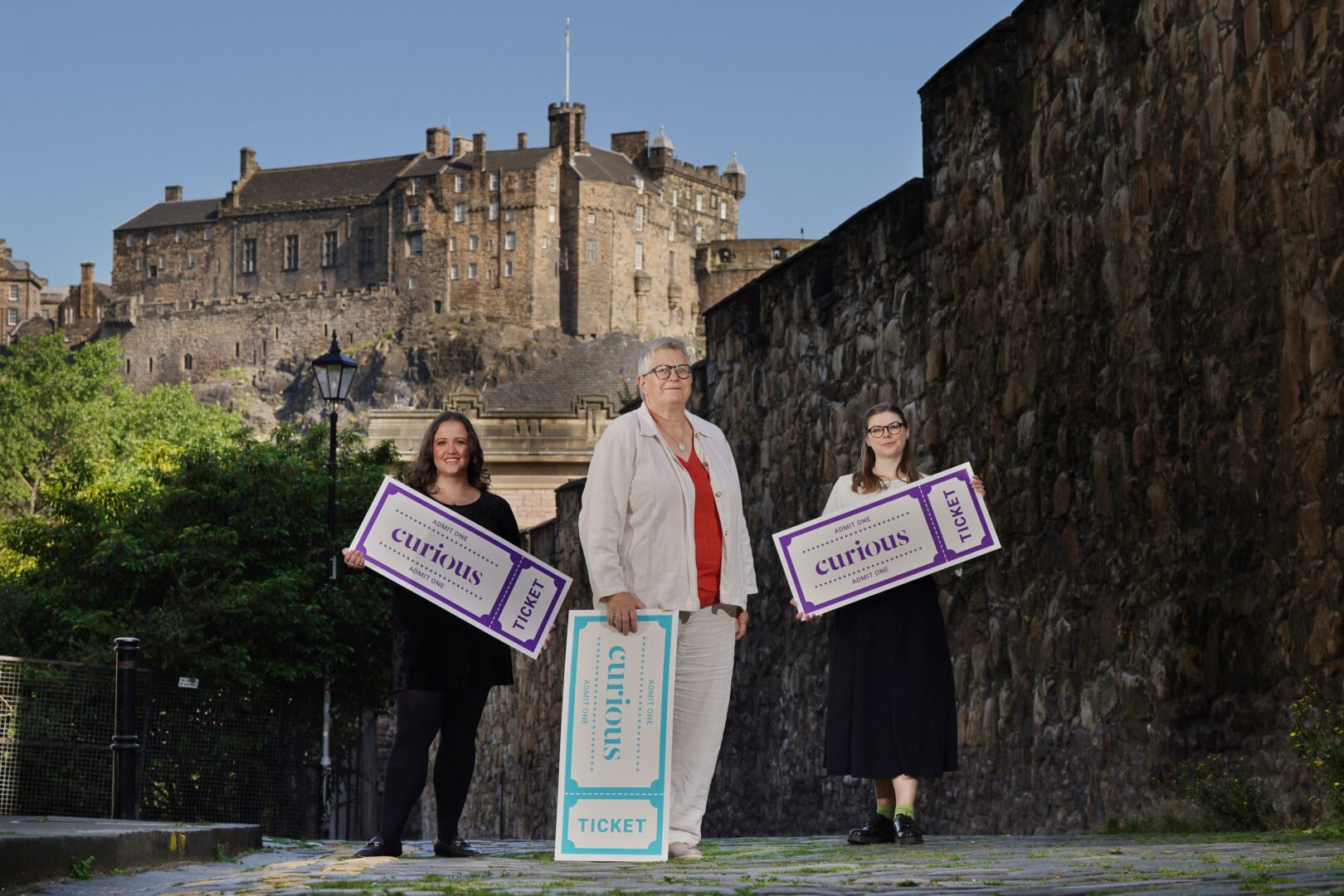 3 women holding over-sized tickets, standing against the backdrop of a castle.