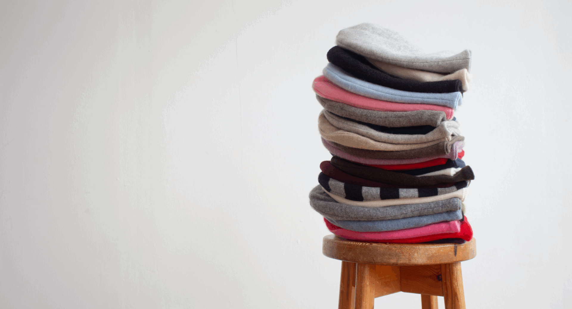 A wooden stool with a pile of woollen items.