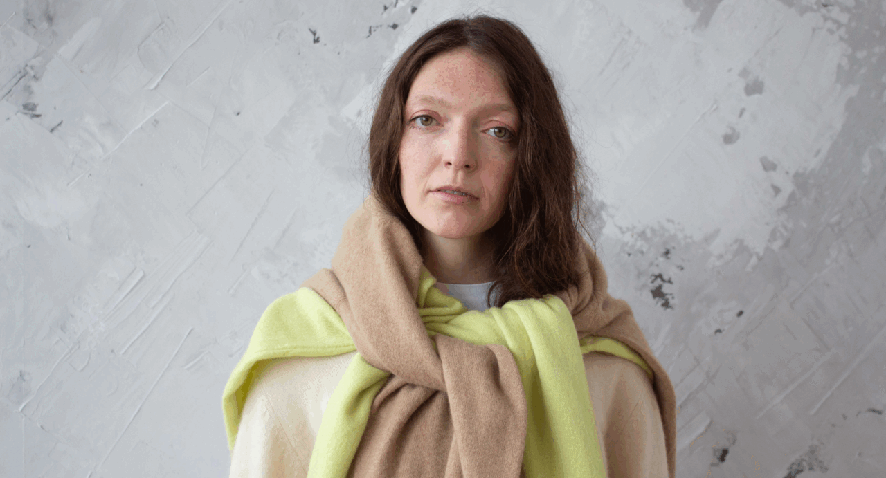 A women with long brown hair with a yellow and a brown jumper draped over her shoulders.