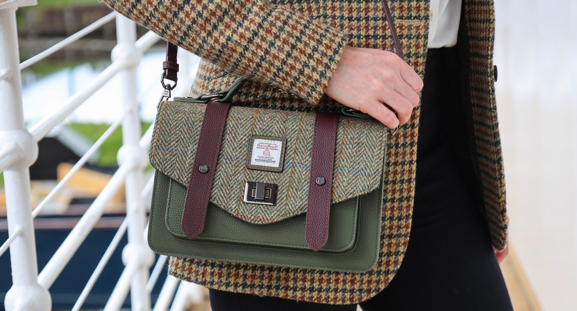 Close-up of a person holding a purple, brown and green tweed handbag.