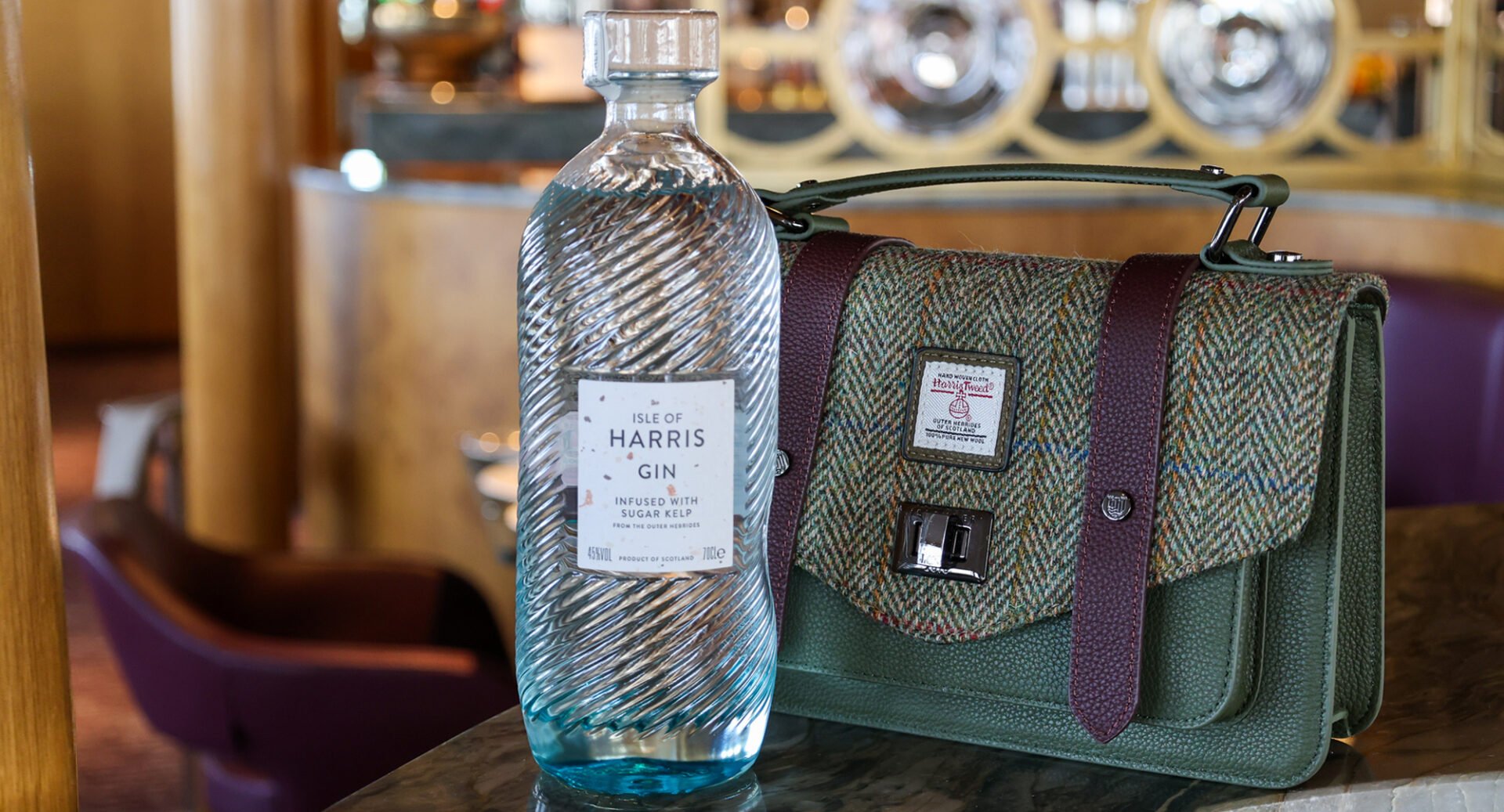 Close-up of a clear glass bottle, labelled Isle of Harris Gin, and a green, purple and brown tweed handbag.