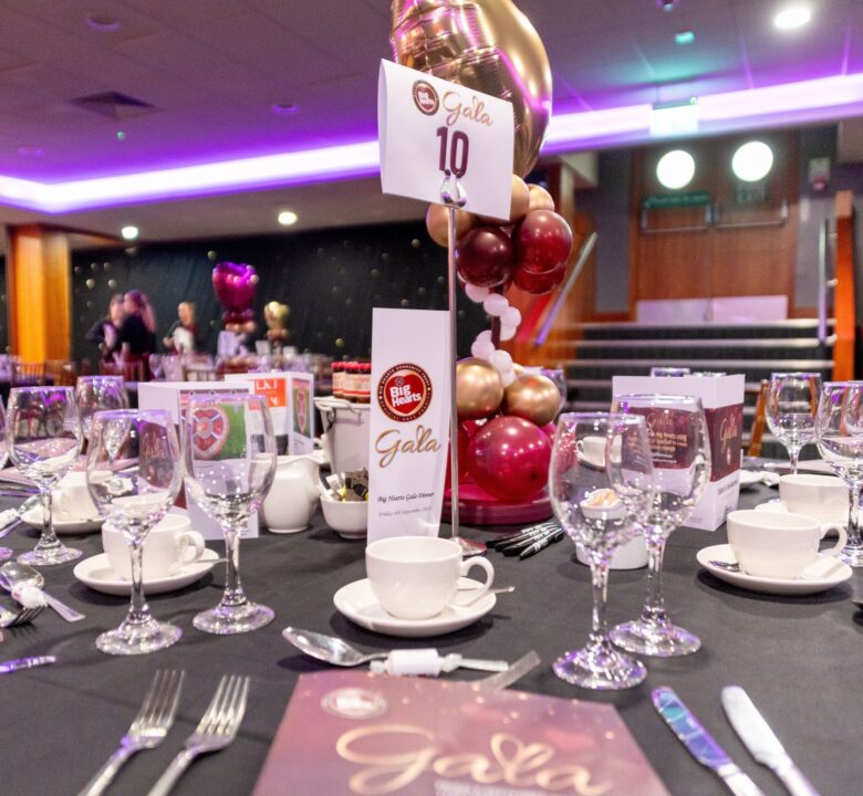 A table set with wine glasses, cups and saucers and cutlery. In the middle is a large display of red and gold balloons.