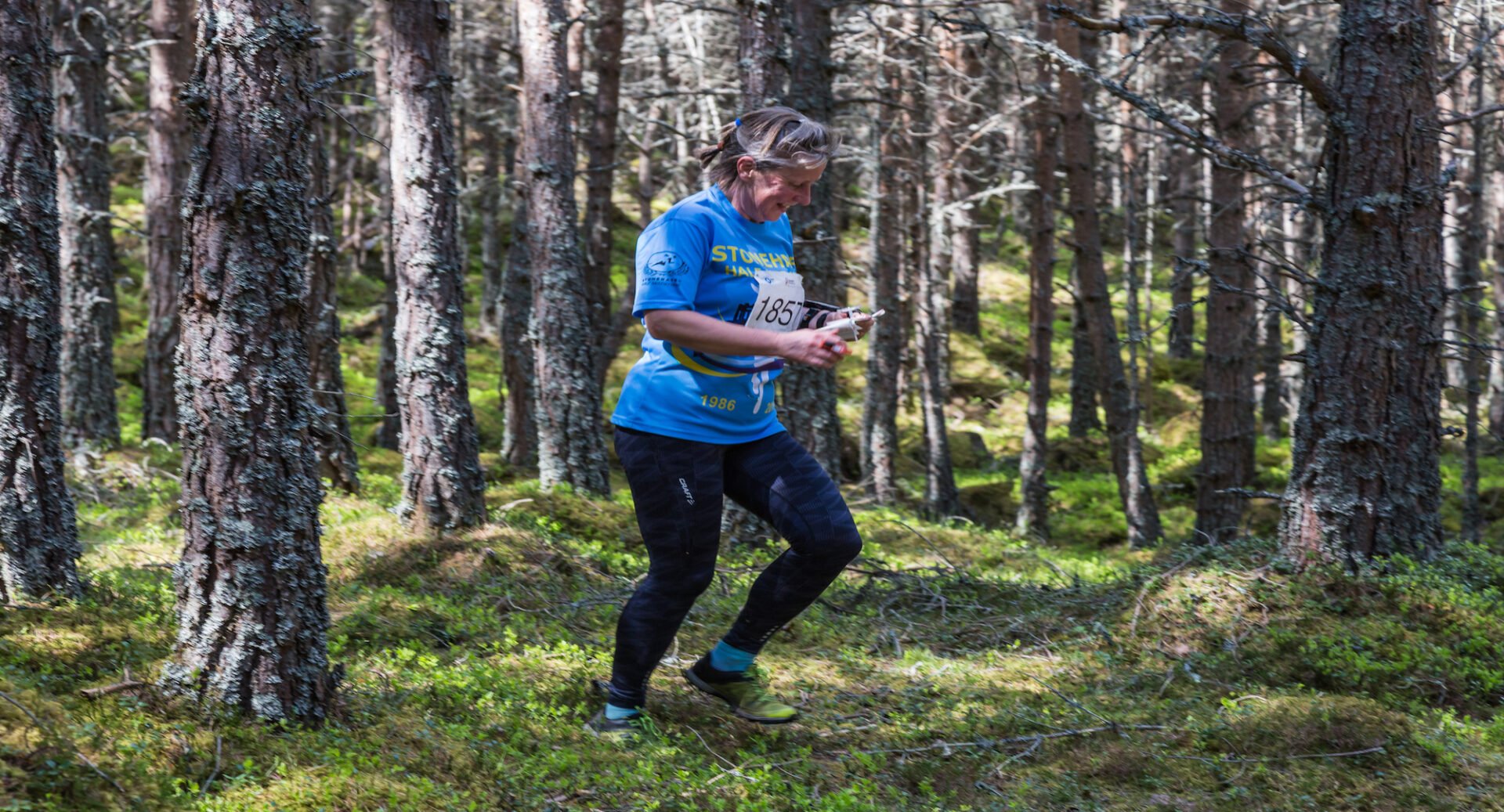 Women in a blue t-shirt and black leggings running through a wooded area.