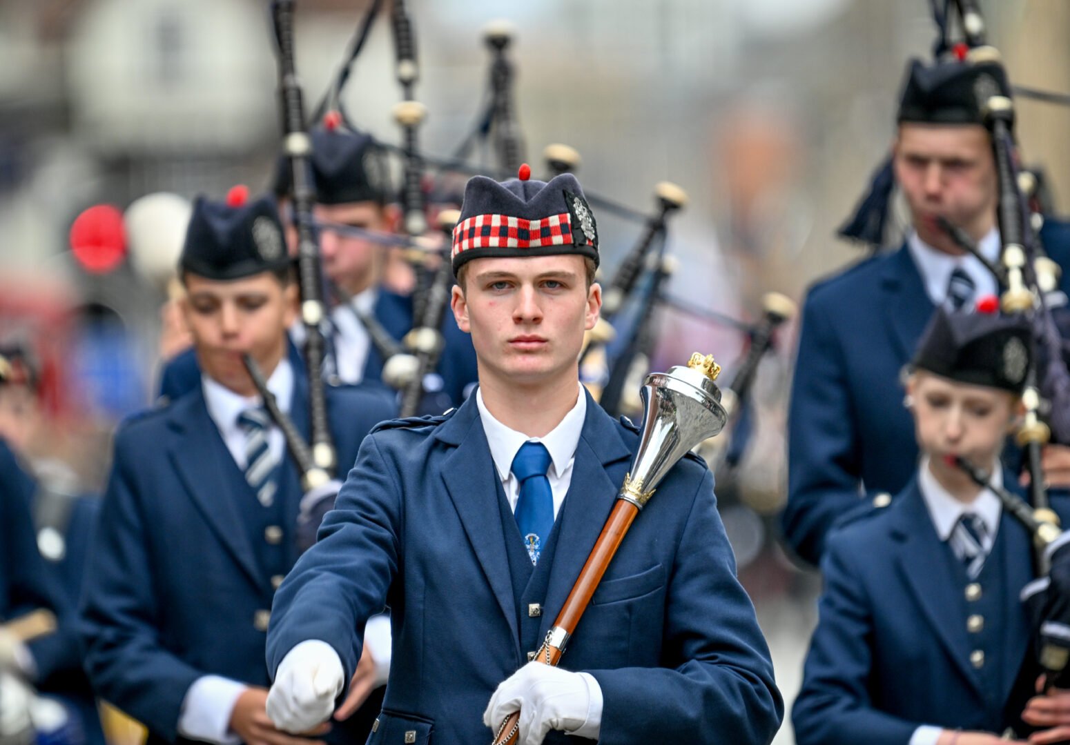 Close up of the Pipe Major with the pipe band dressed in blue behind