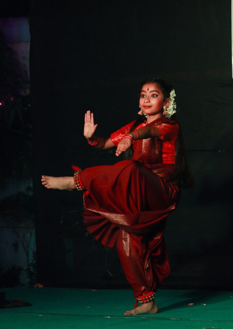 A young girl dressed in a red, traditional Indian outfit, dancing