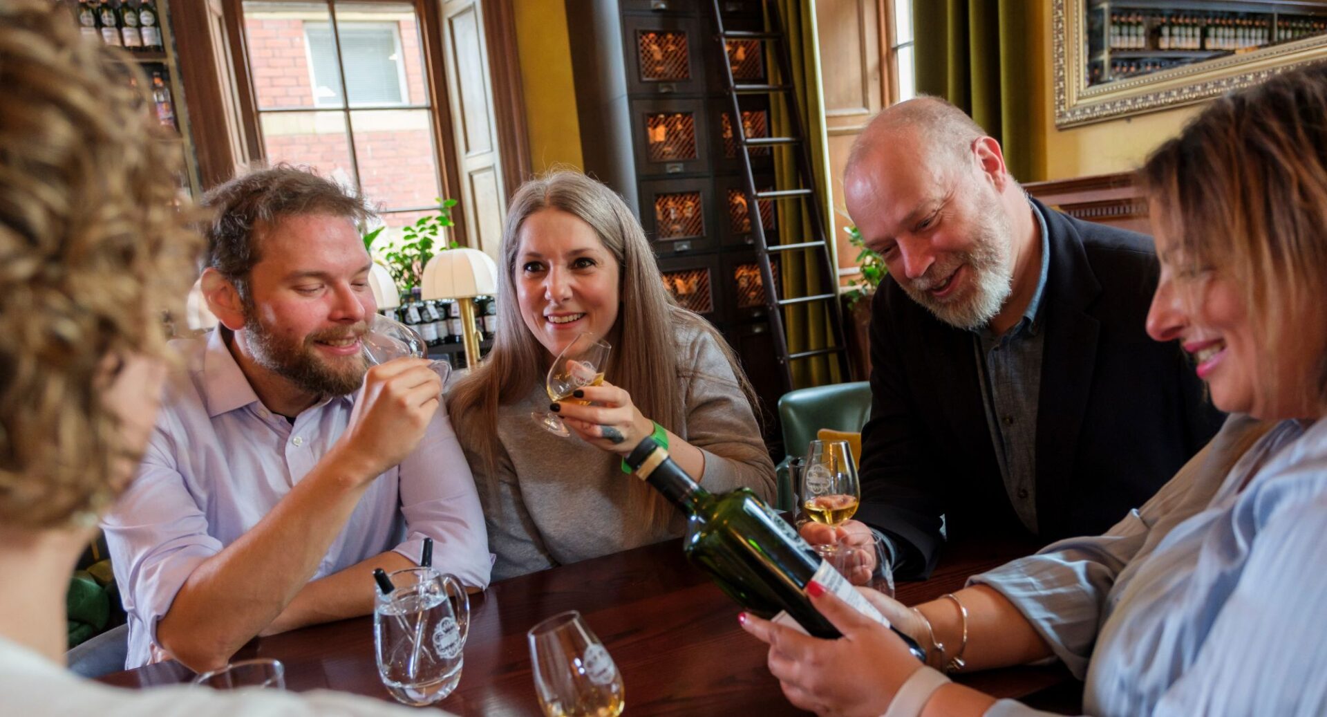 Group of people seated round a table, with glasses and a bottle of whisky.