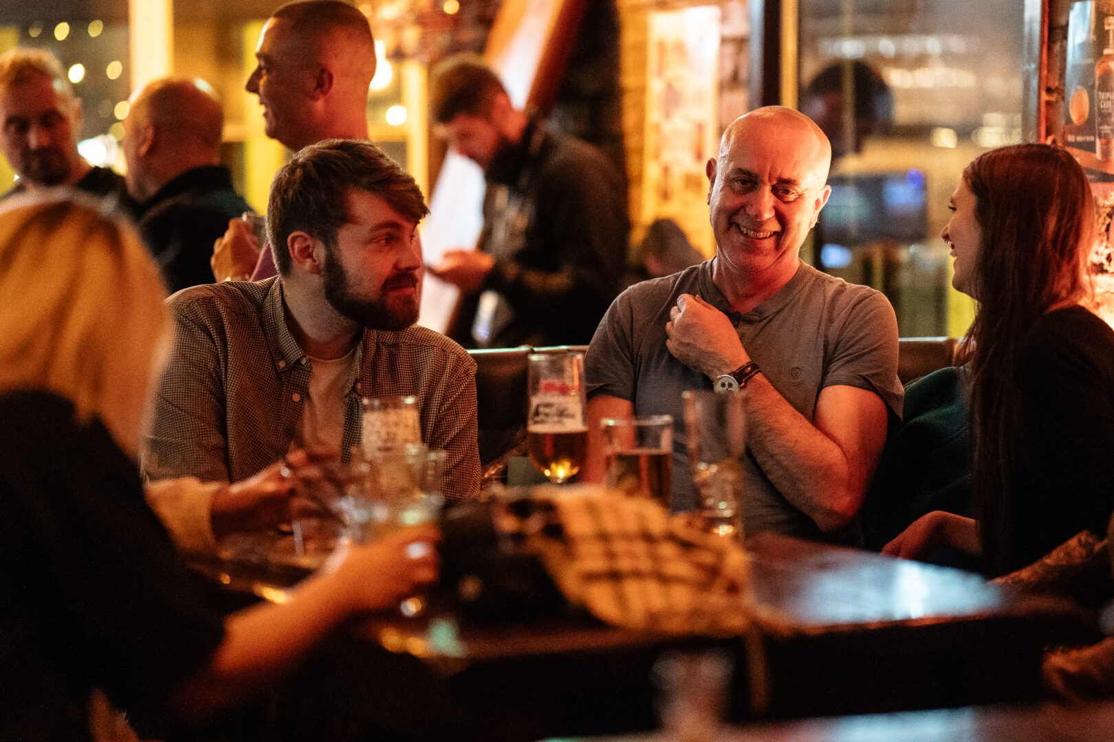 3 people seated round a table in a bar, laughing.