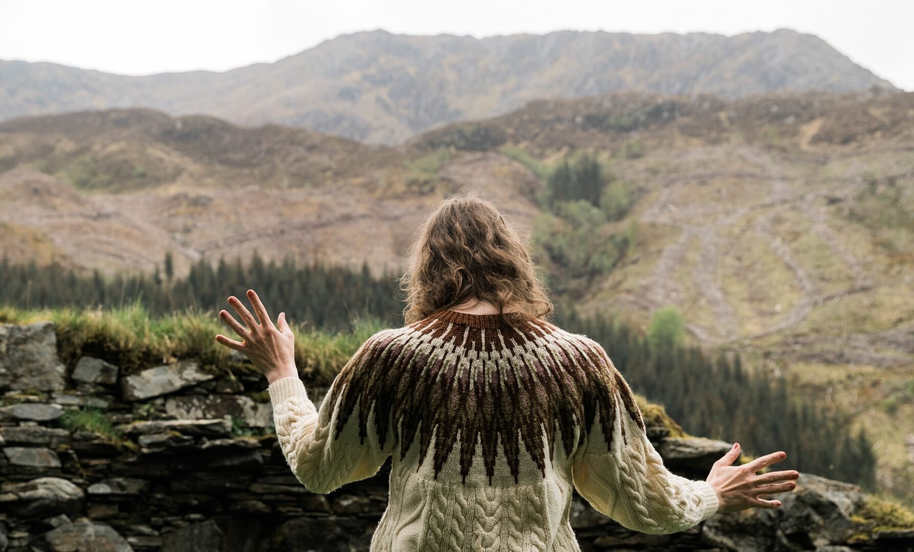 Lady staring over wall at hills in the distance.