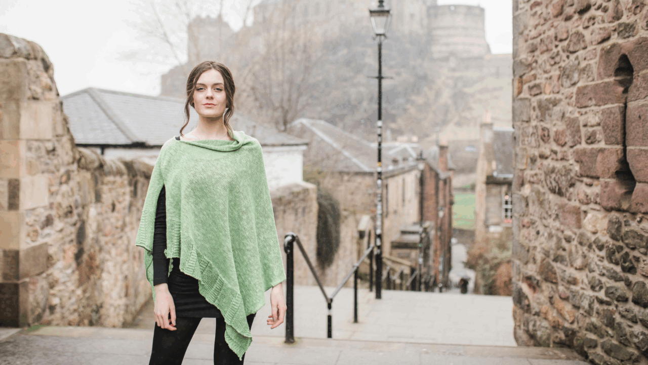 A woman wearing a Bill Baber Knitwear shawl at the top of stairs in front of Edinburgh Castle at the Edinburgh Vennel,© Bill Baber Knitwear
