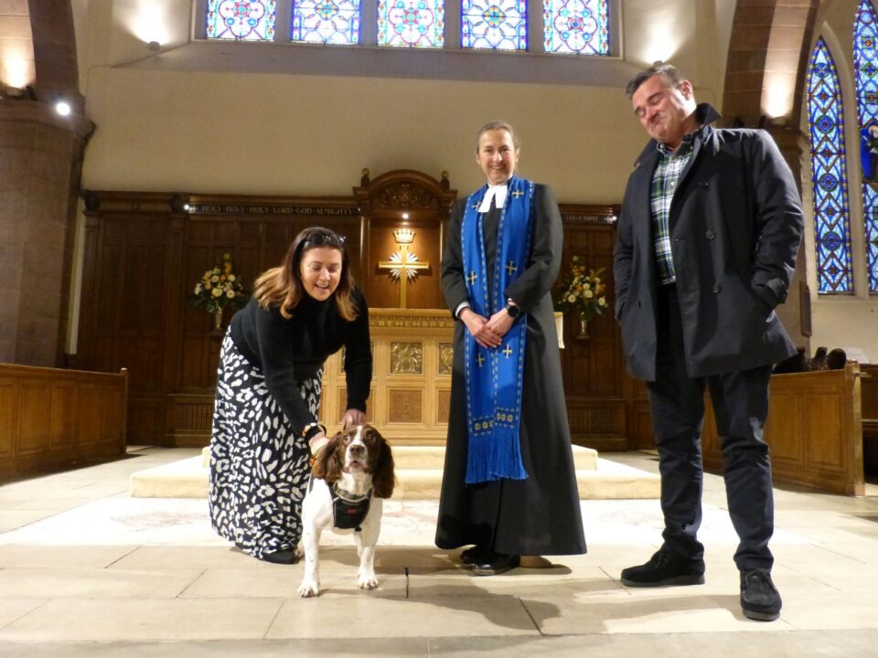 3 people and a dog standing in a church setting.