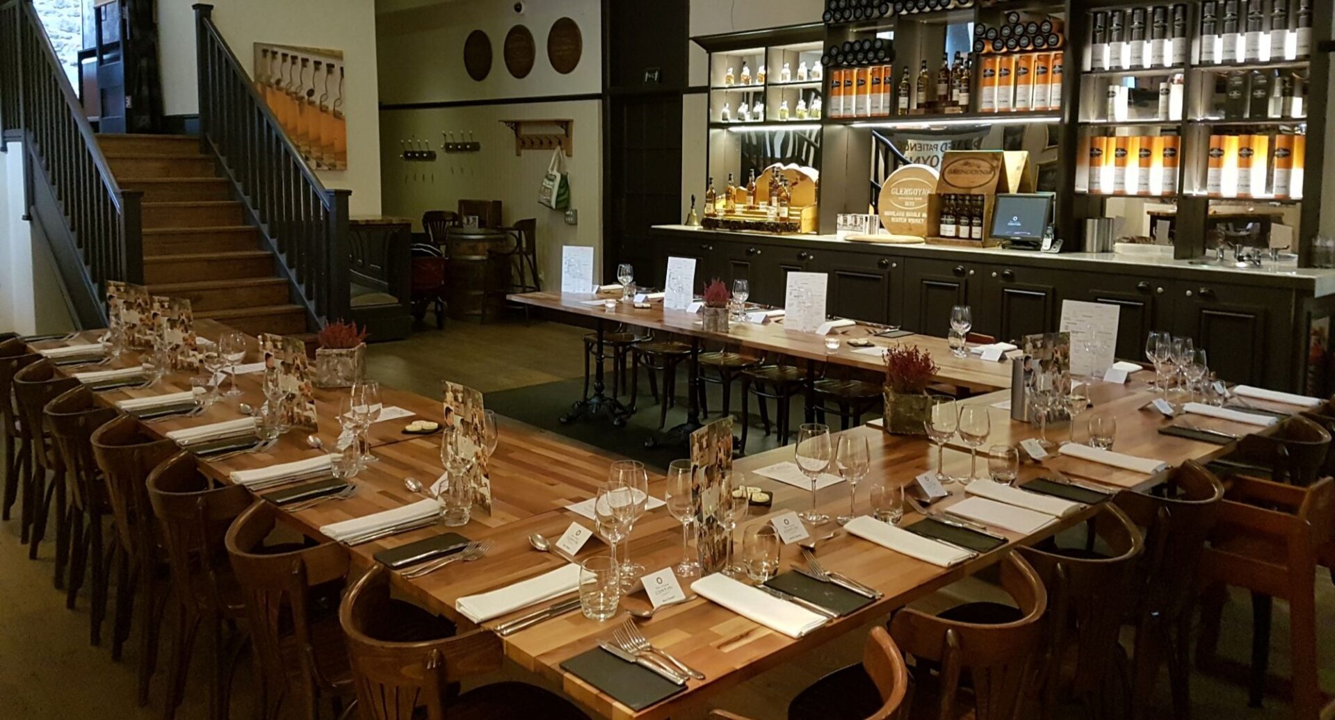 U-shaped table in a restaurant, set with place settings. In the background is a bar area.