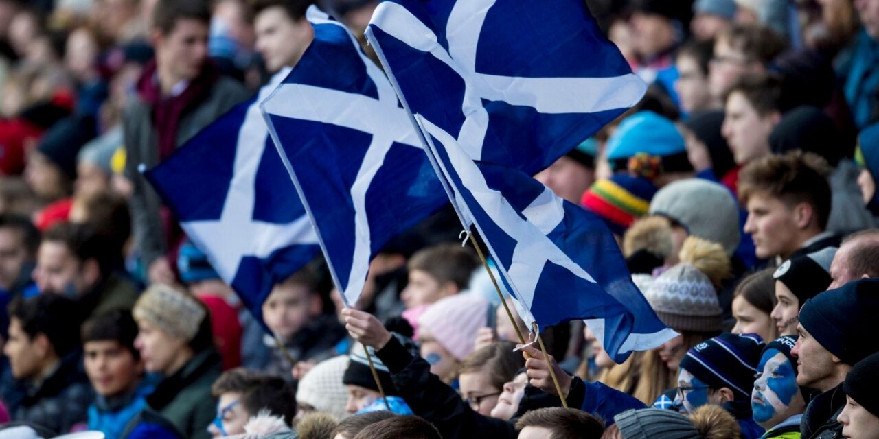 A stadium of people, holding blue and white Scottish flags.