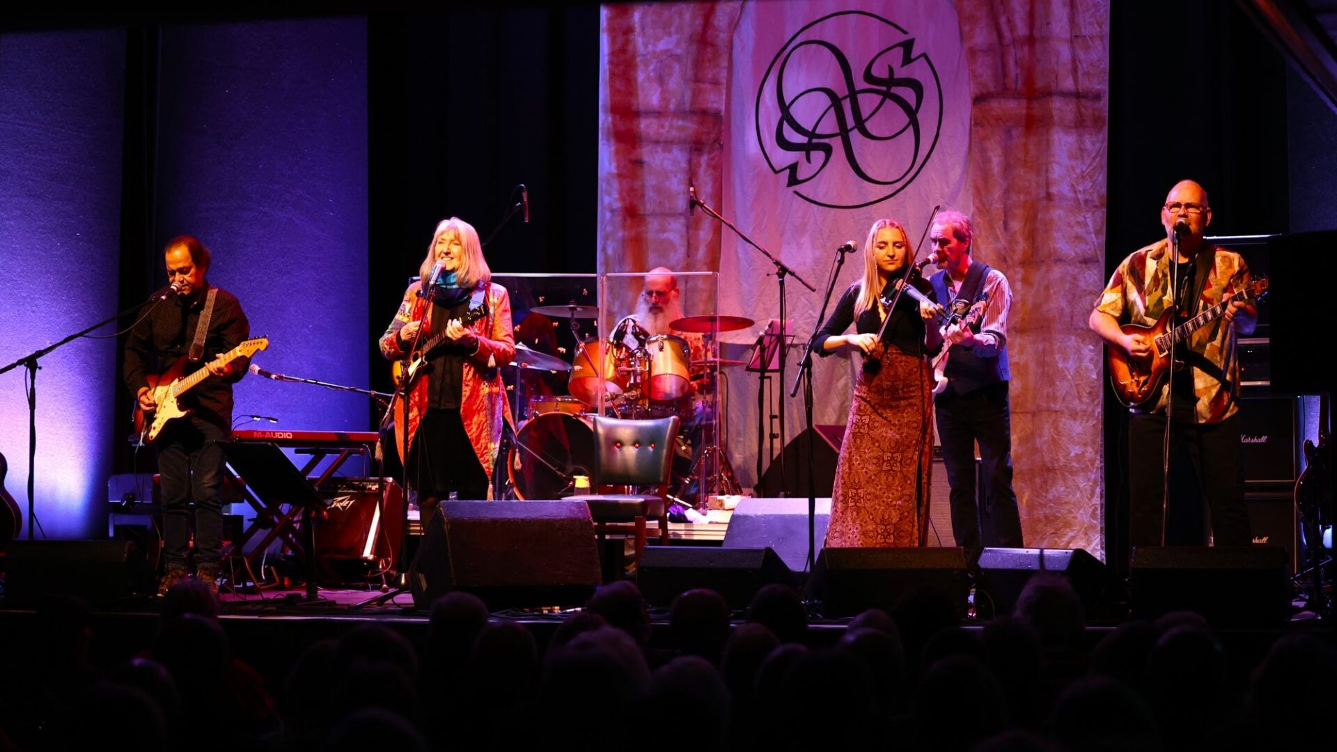Group of people on a stage, with various musical instruments.