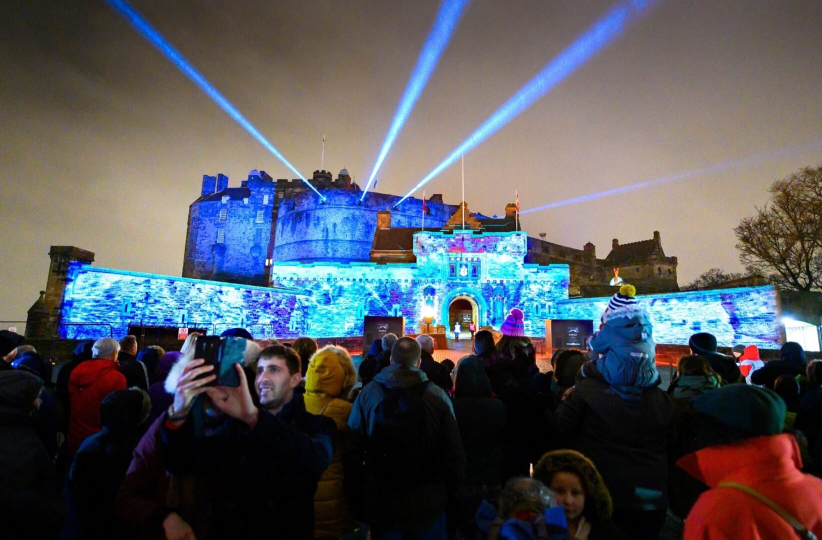 Groups of people standing against a castle building, which is illuminated by a blue light.
