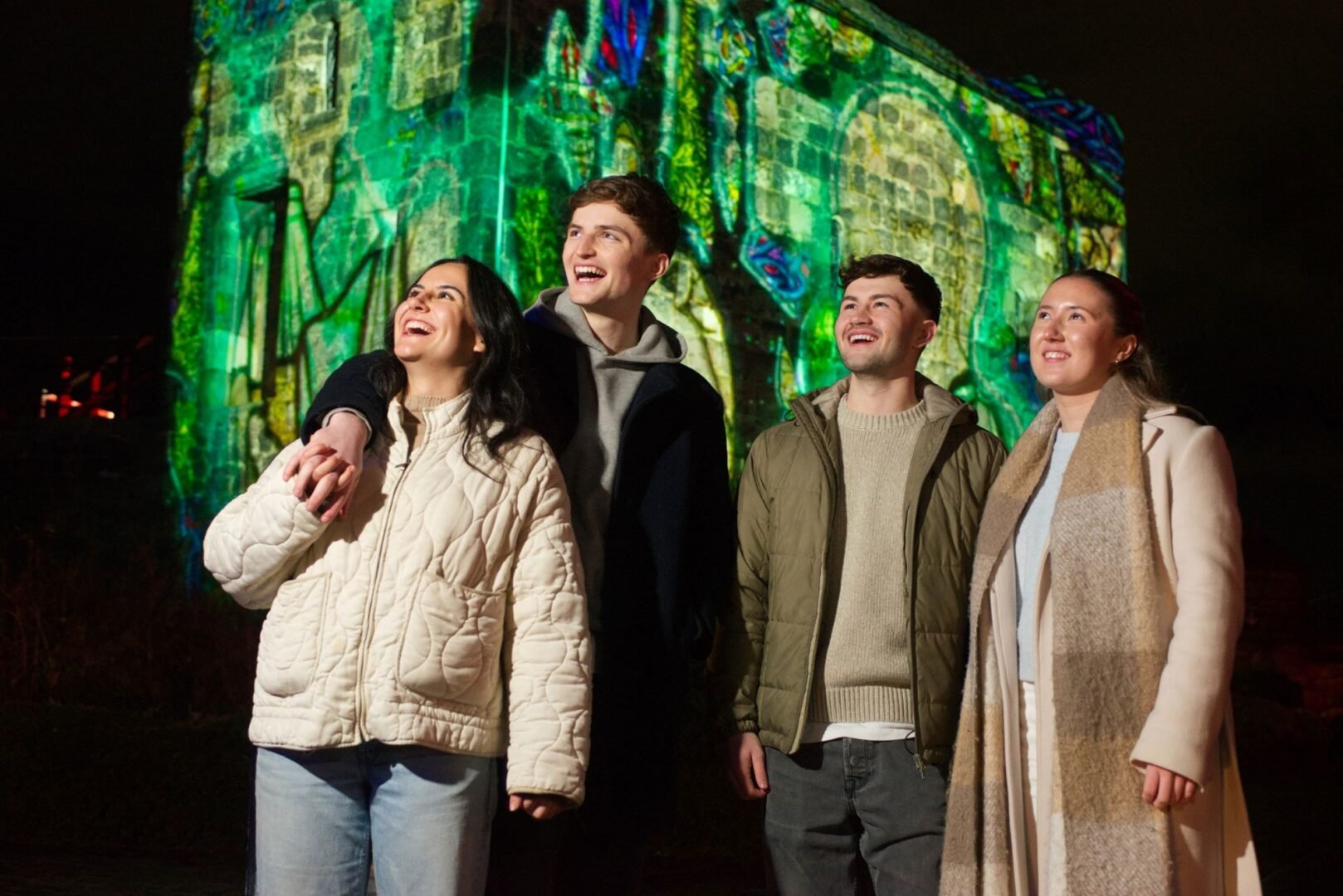 4 people standing outside, against the backdrop of a brightly lit building.