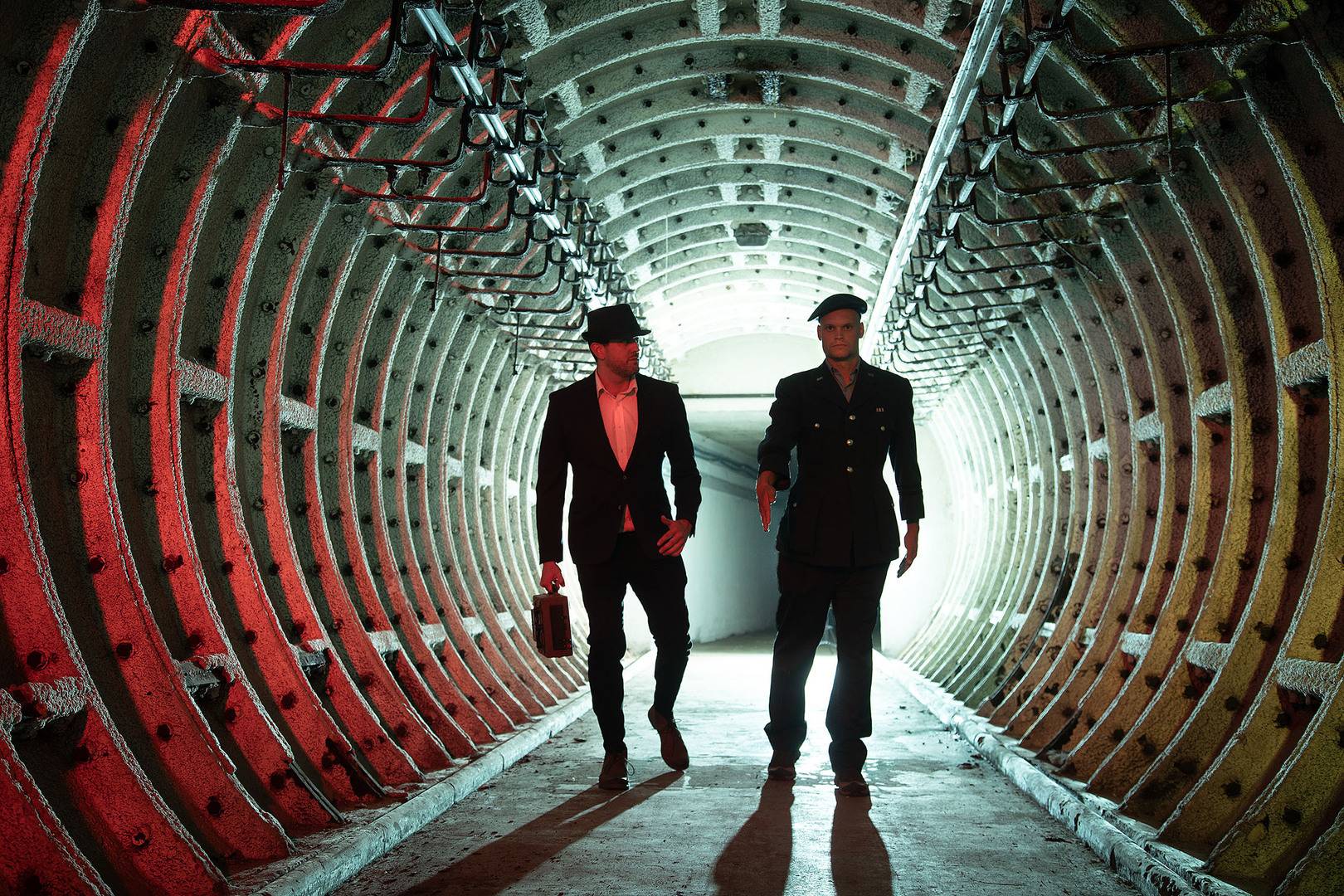 2 men dressed in military and spy outfits walking along tunnel at Edinburgh Nuclear Bunker Tour