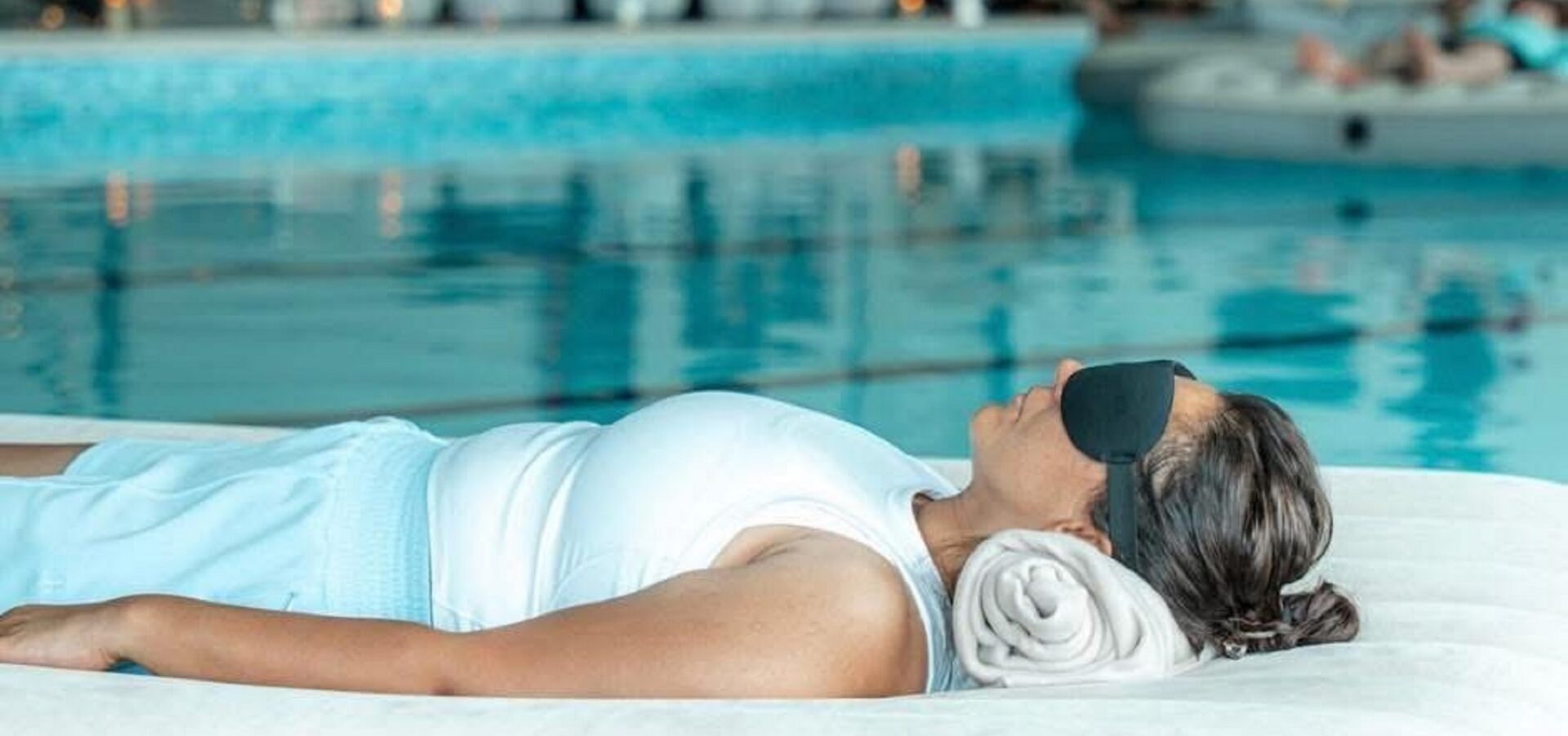Women floating on an airbed in water, with a black mask over her eyes.