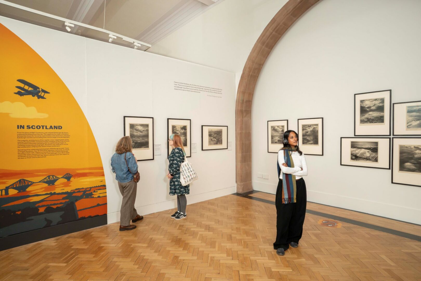 3 people standing in a gallery space, with framed photos hanging on the walls.