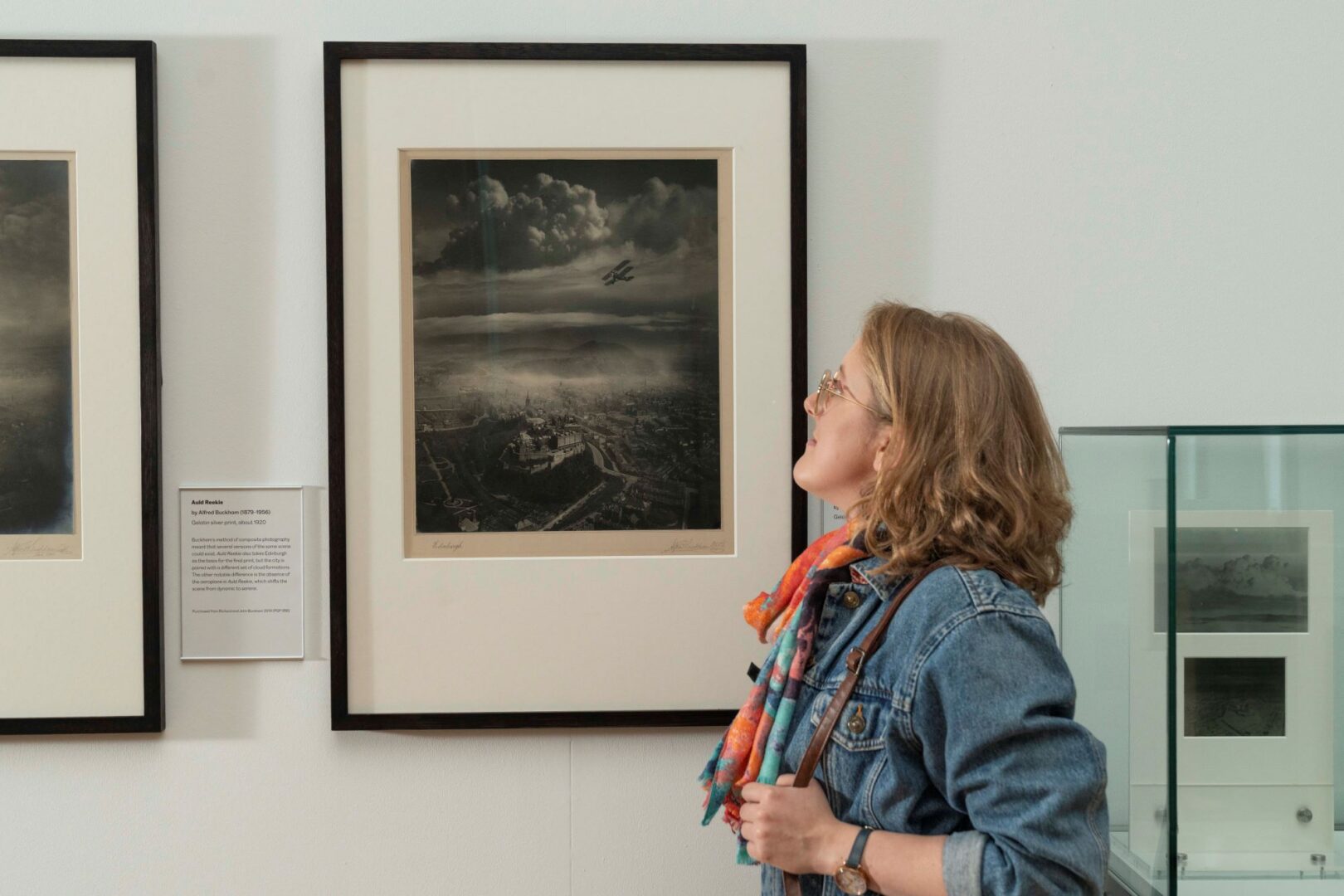Woman looking at a framed photo on a wall.